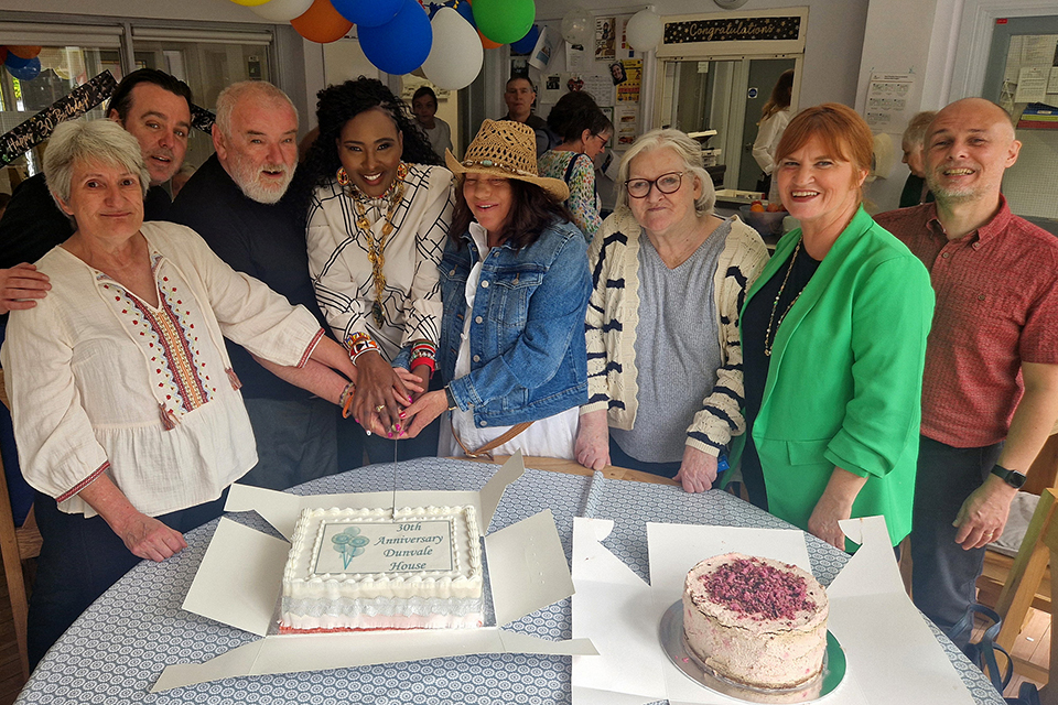 A group of people gathered around a table as they cut a cake marking the celebration.